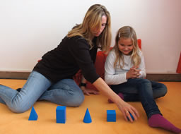 Astrid Ablaßmayer sitzt mit einem Kind vor geometrischen Figuren